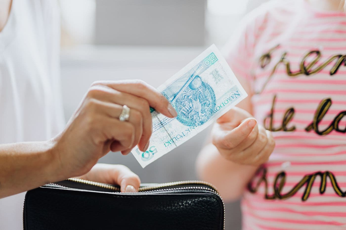 Dłonie przekazujące banknot 50 złotych jako kieszonkowe.